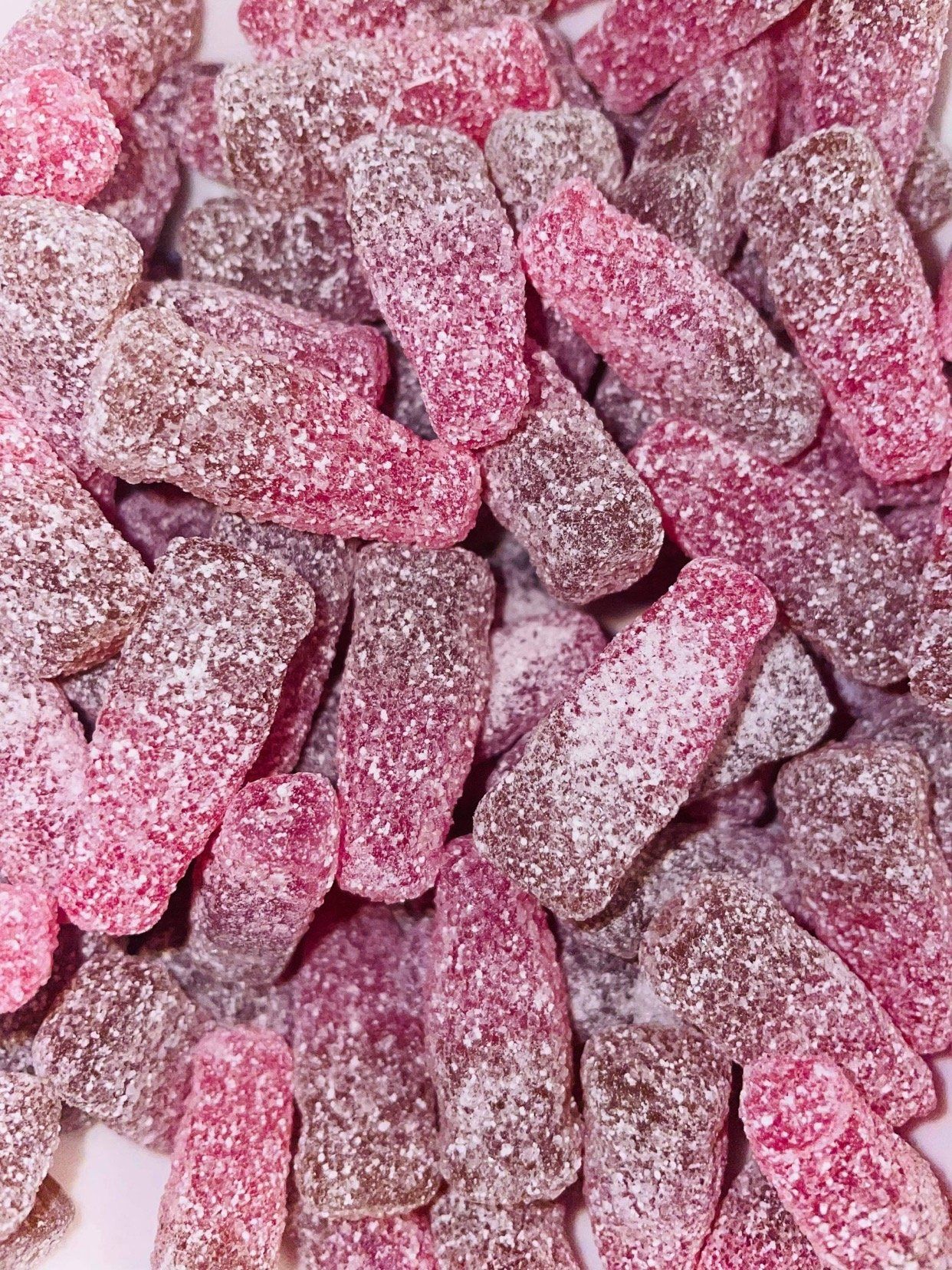 A pile of pink and brown gummy bottles on a white surface.