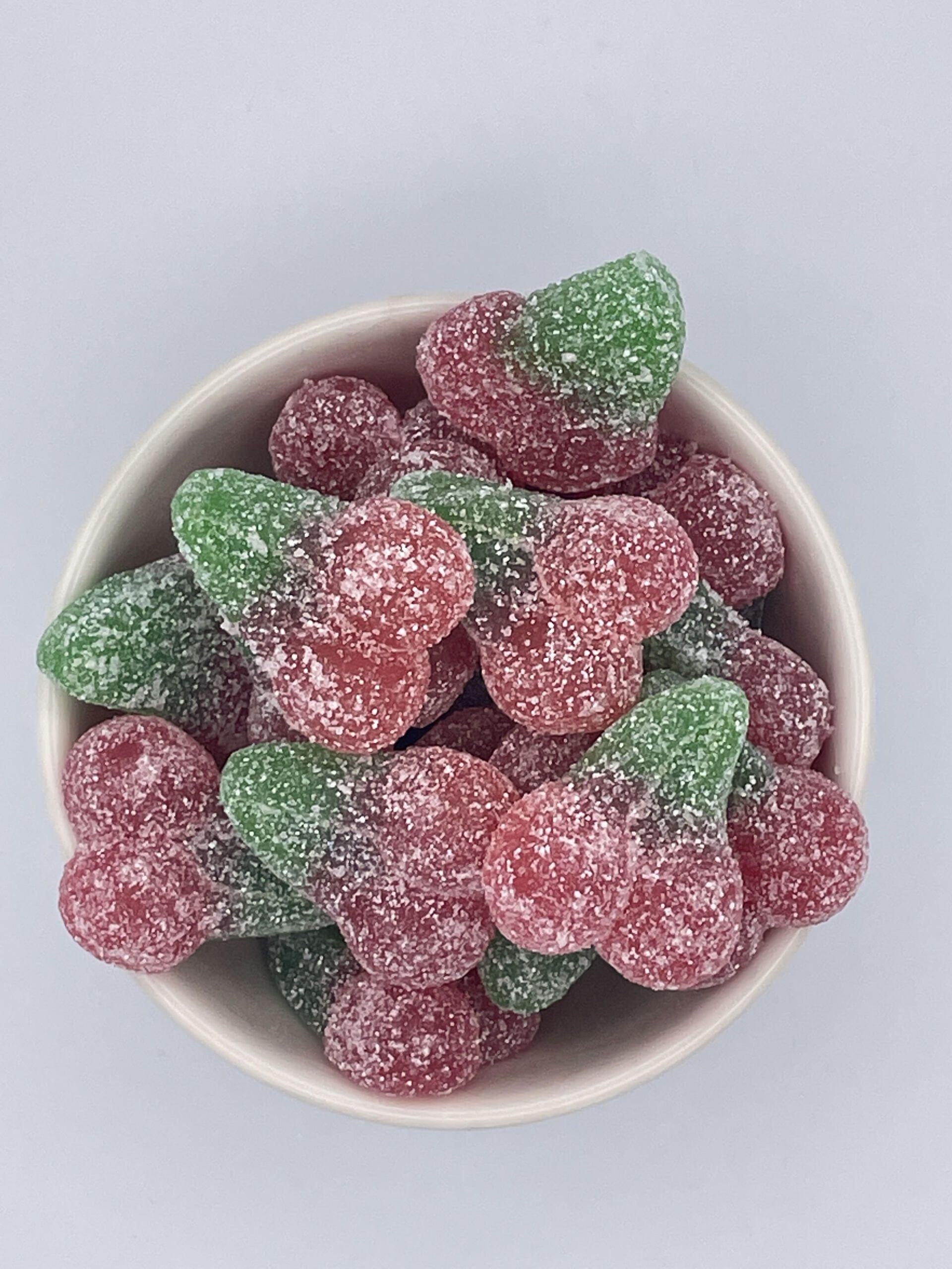 A bowl filled with red and green gummy cherries