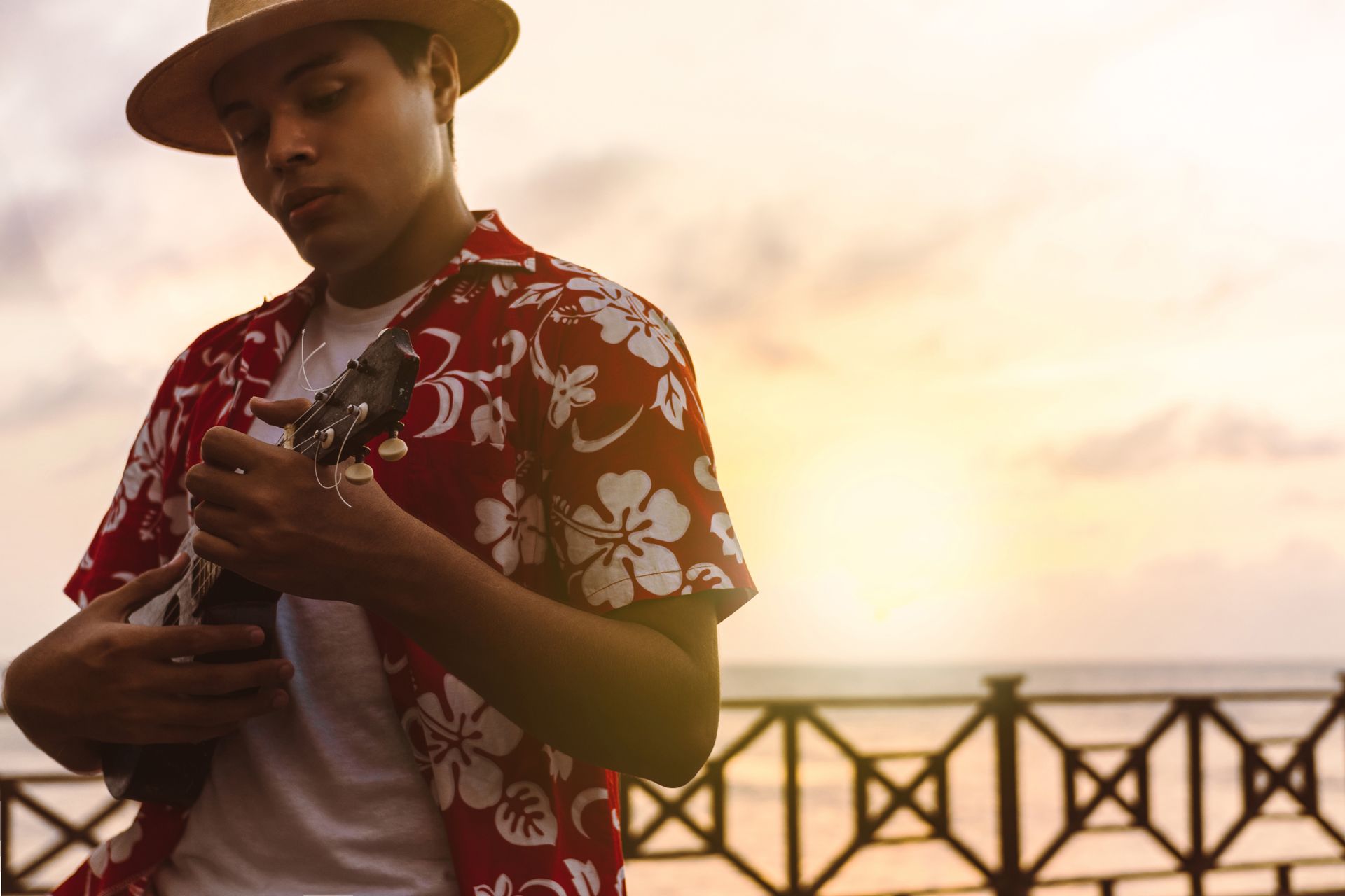 a man in a Hawaiian shirt and hat is holding a gutair .