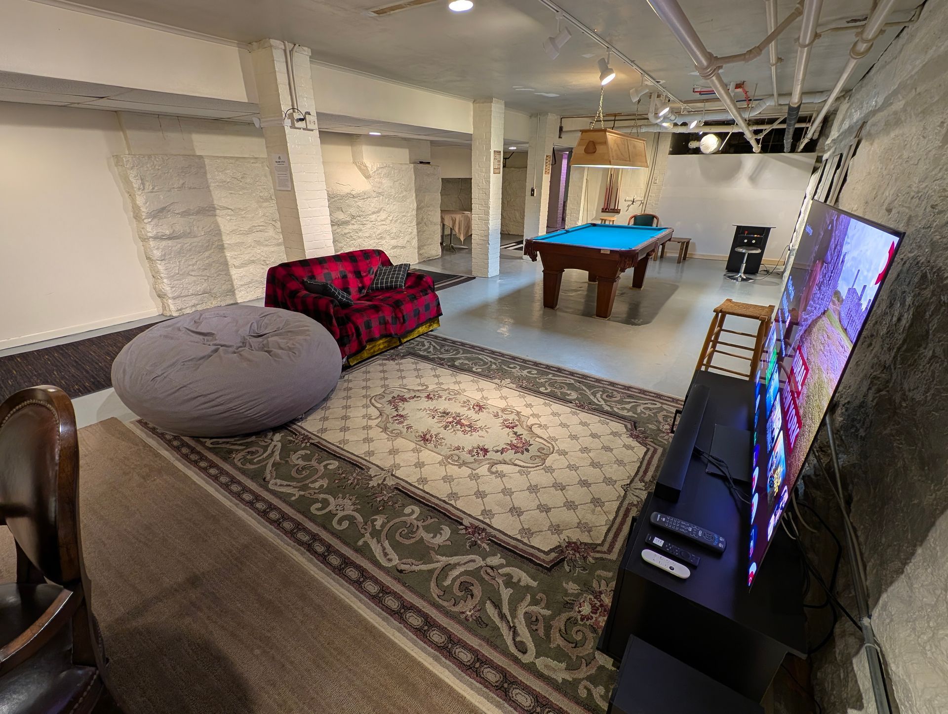 Basement game room featuring a pool table, red sofa, gray beanbag chair, area rug, and a large wall-mounted television.