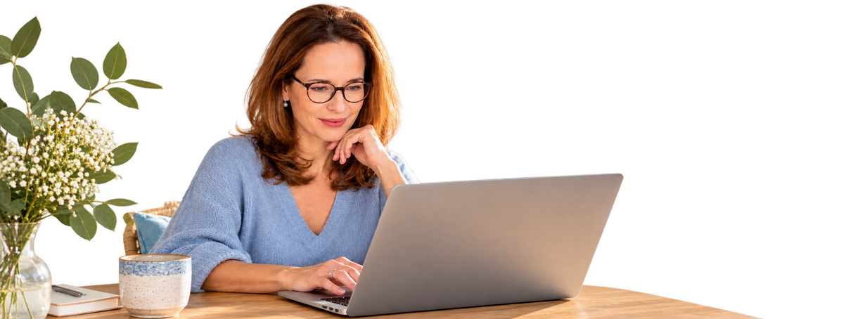 Eine Frau arbeitet an einem Schreibtisch an einem Laptop. In der Nähe stehen eine Pflanze und ein Notizbuch.