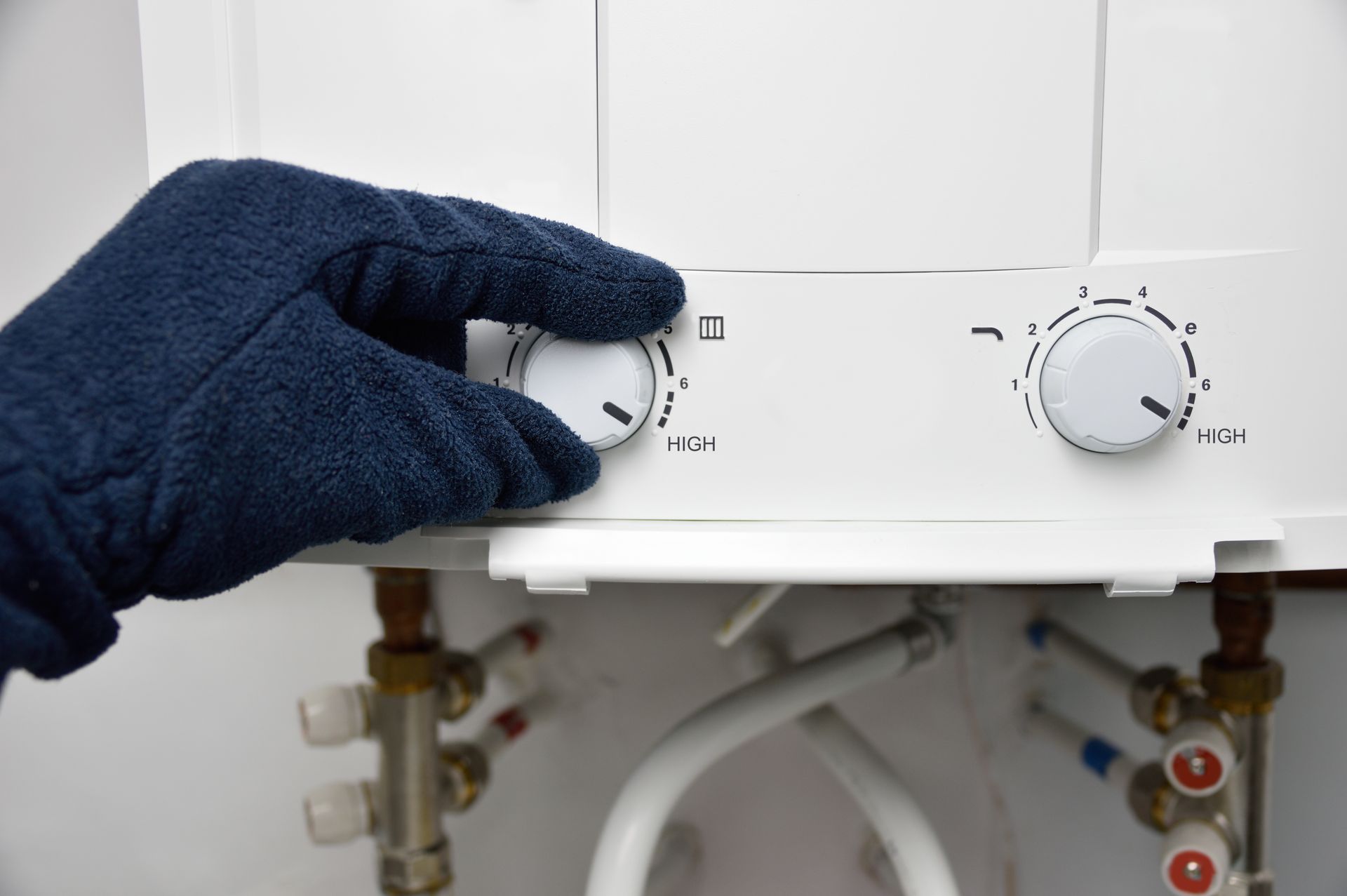 Gloved hand turning a dial on a white water heater, close-up shot.