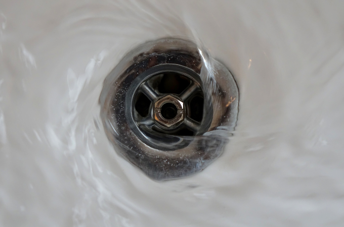 A plumber is fixing a sink in a kitchen while a woman sits on the floor.