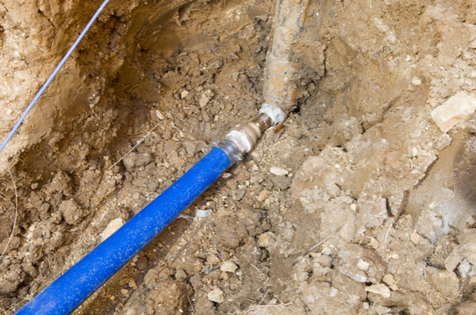 A man is working on blue pipes in the dirt.