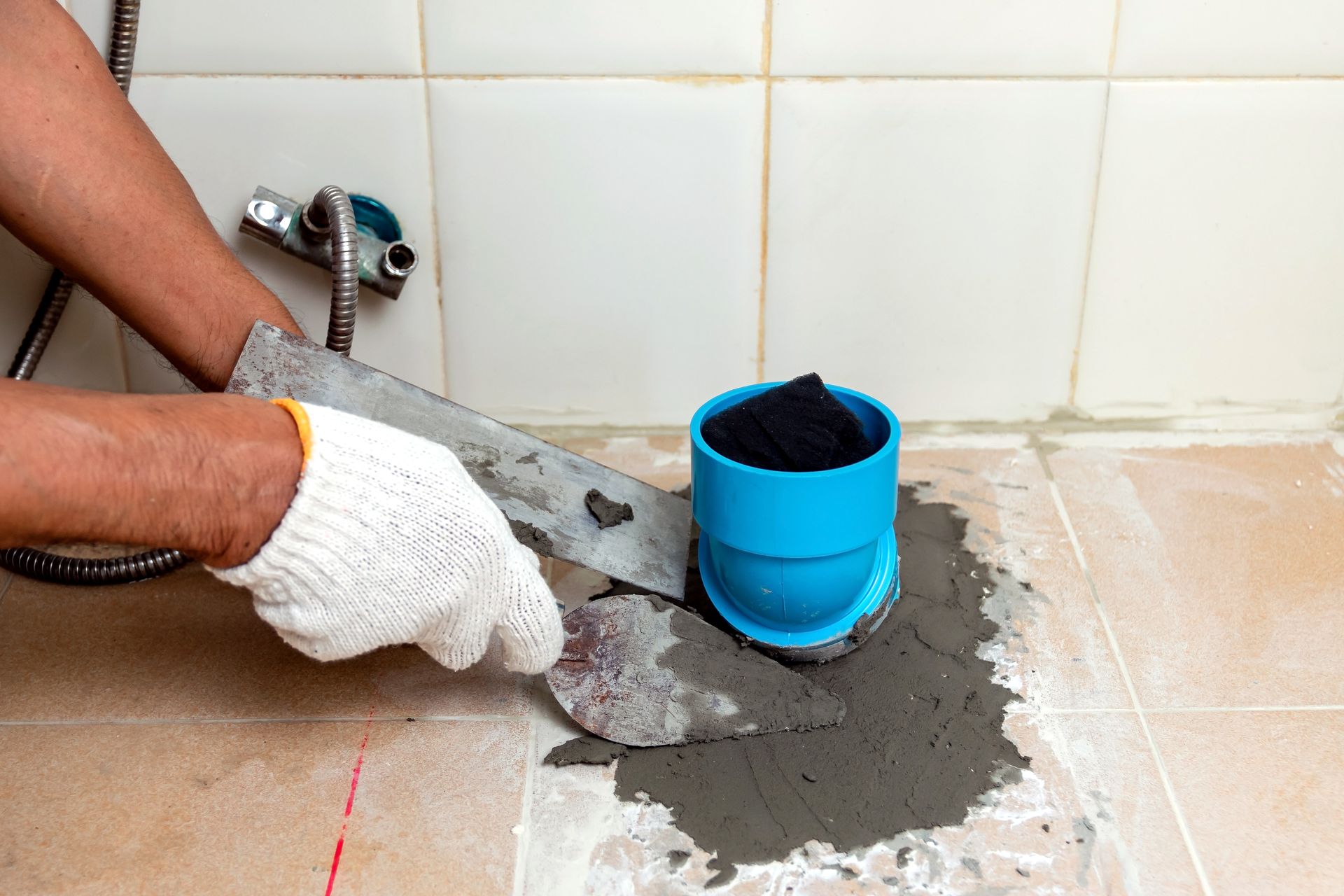 A person is using a spatula to spread cement on the floor in a bathroom.