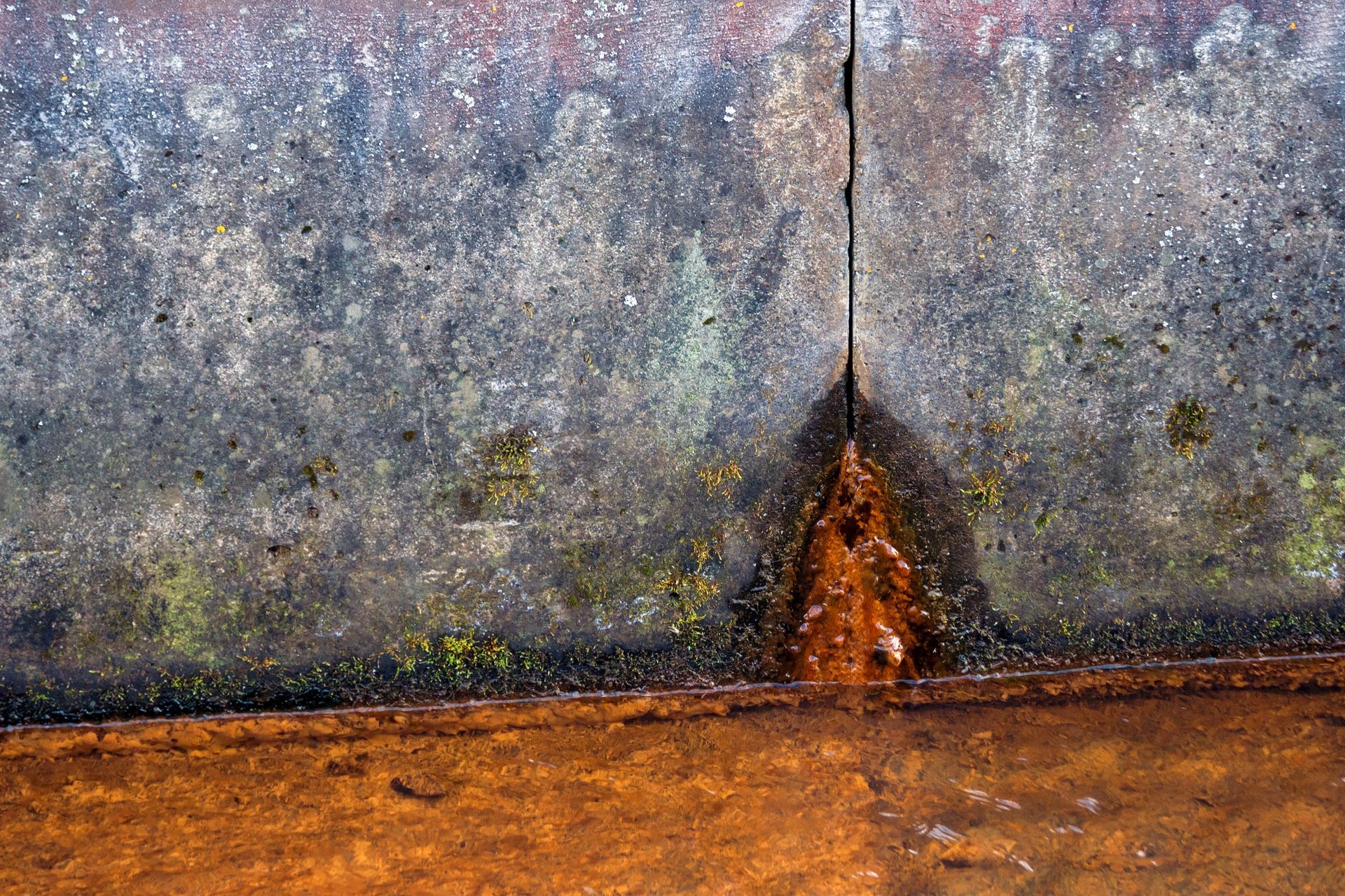 Rusty metal wall with a dark vertical seam above a brown, weathered surface