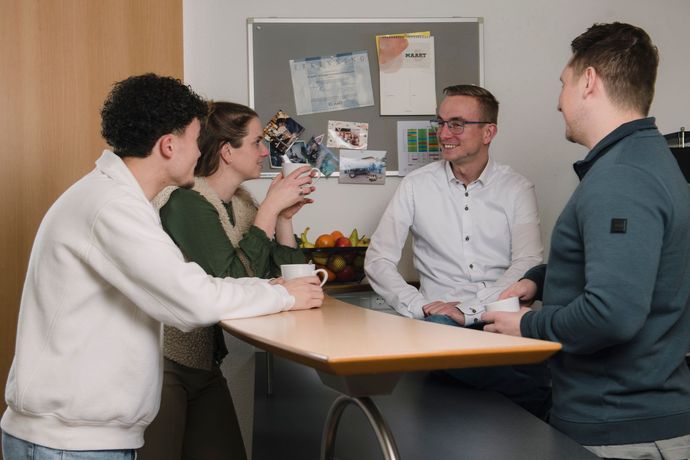 Een groep mensen zit rond een tafel en drinkt koffie.