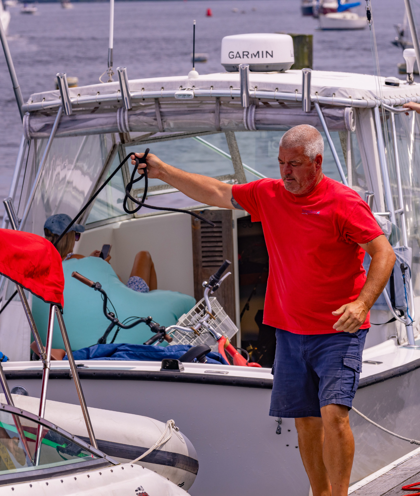 A man in a red shirt is standing next to a boat with a garmin antenna on top of it.