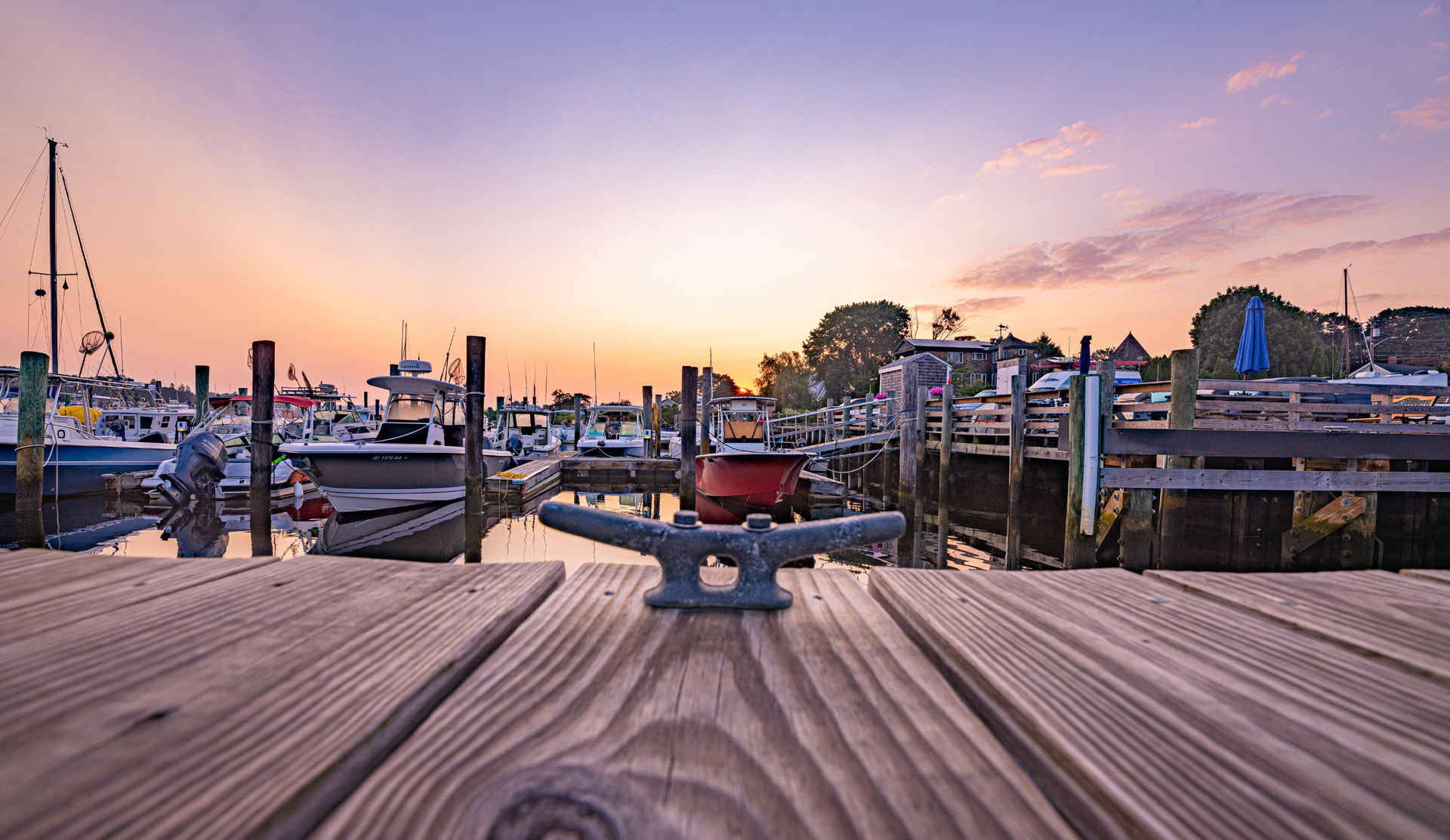 A wooden dock with boats docked at a marina at sunset.