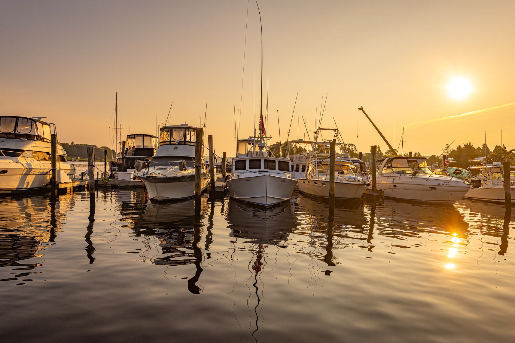 A row of boats are docked in a marina at sunset.