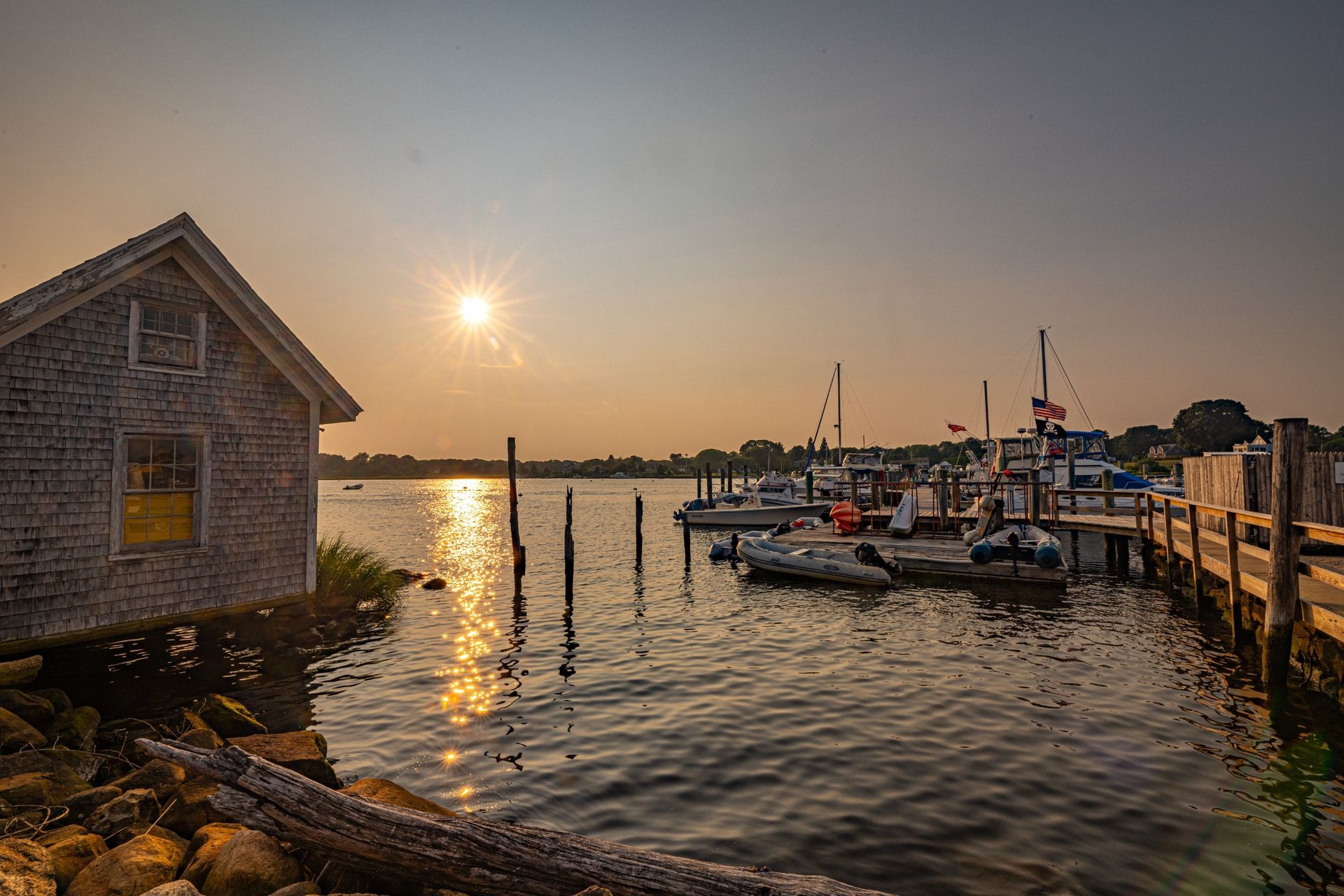 The sun is setting over a harbor with boats docked and a shed in the foreground.