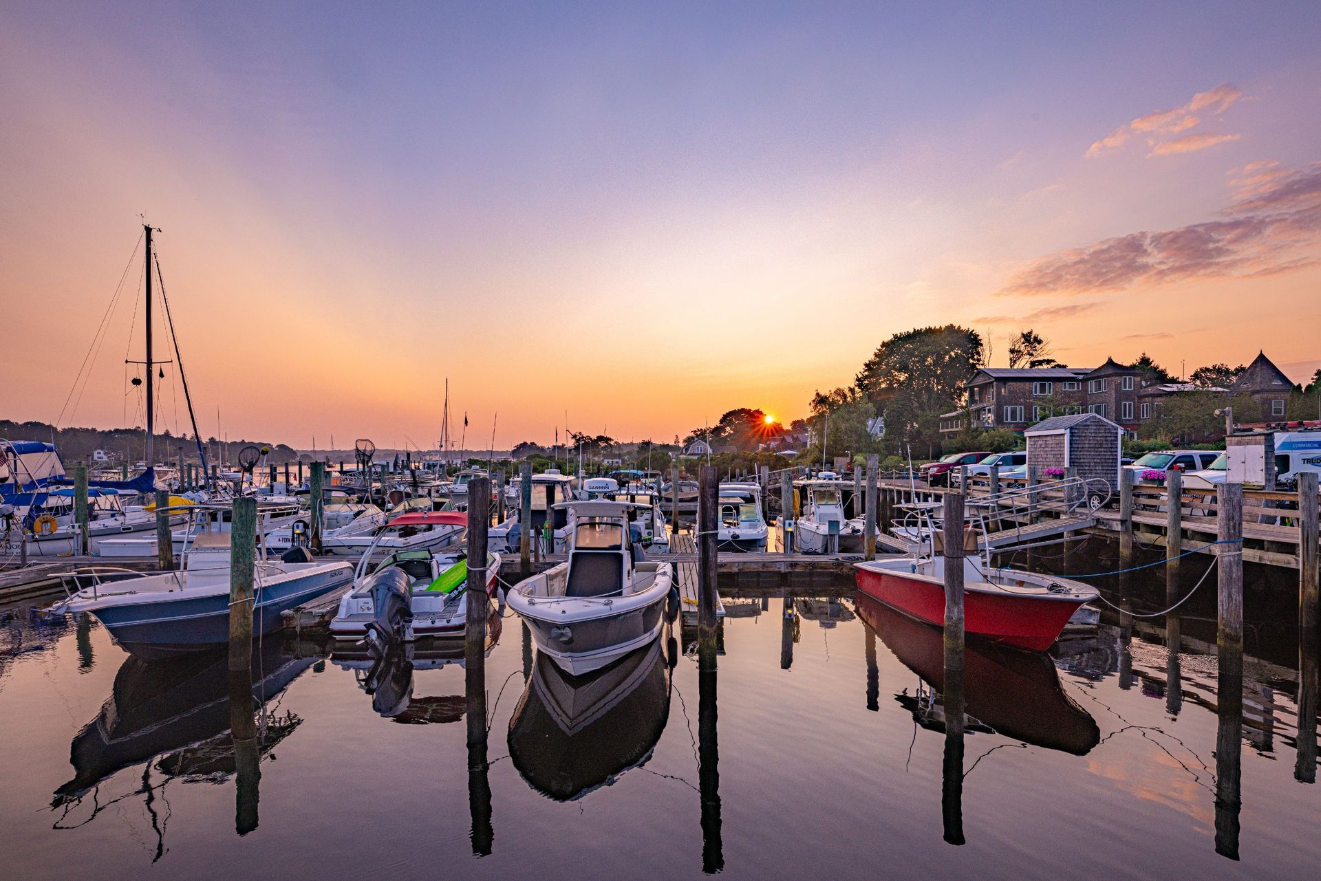 A row of boats are docked in a marina at sunset.