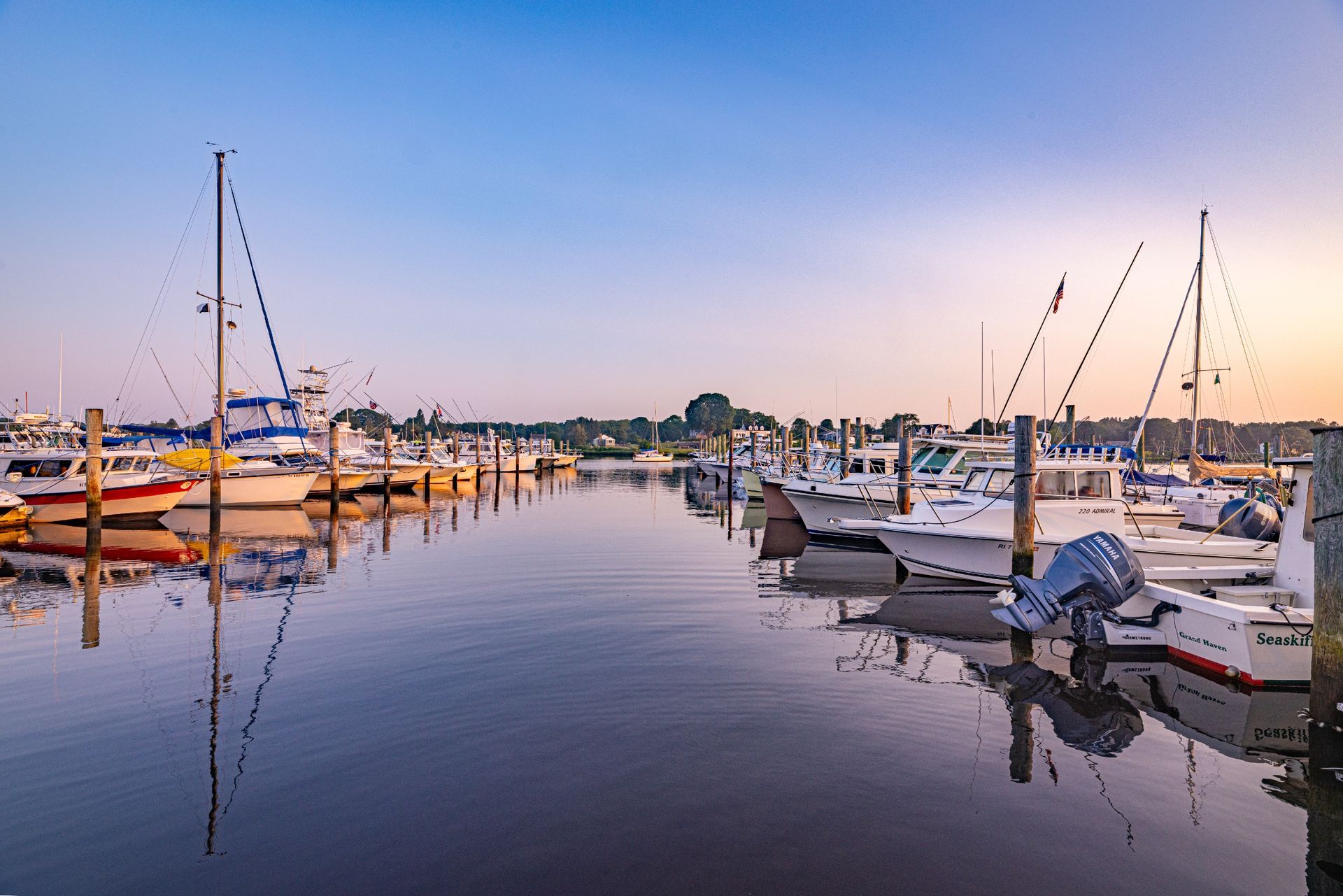 A row of boats are docked in a marina at sunset.