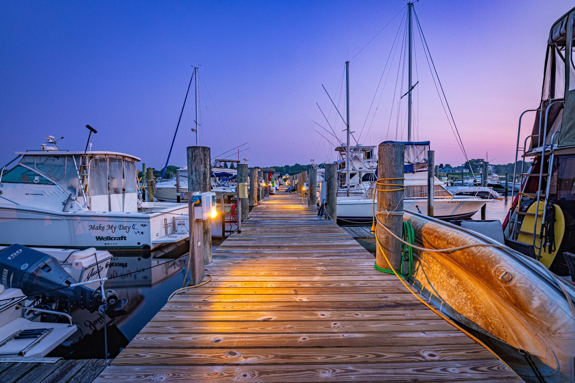 A wooden dock with boats docked at a marina at sunset.
