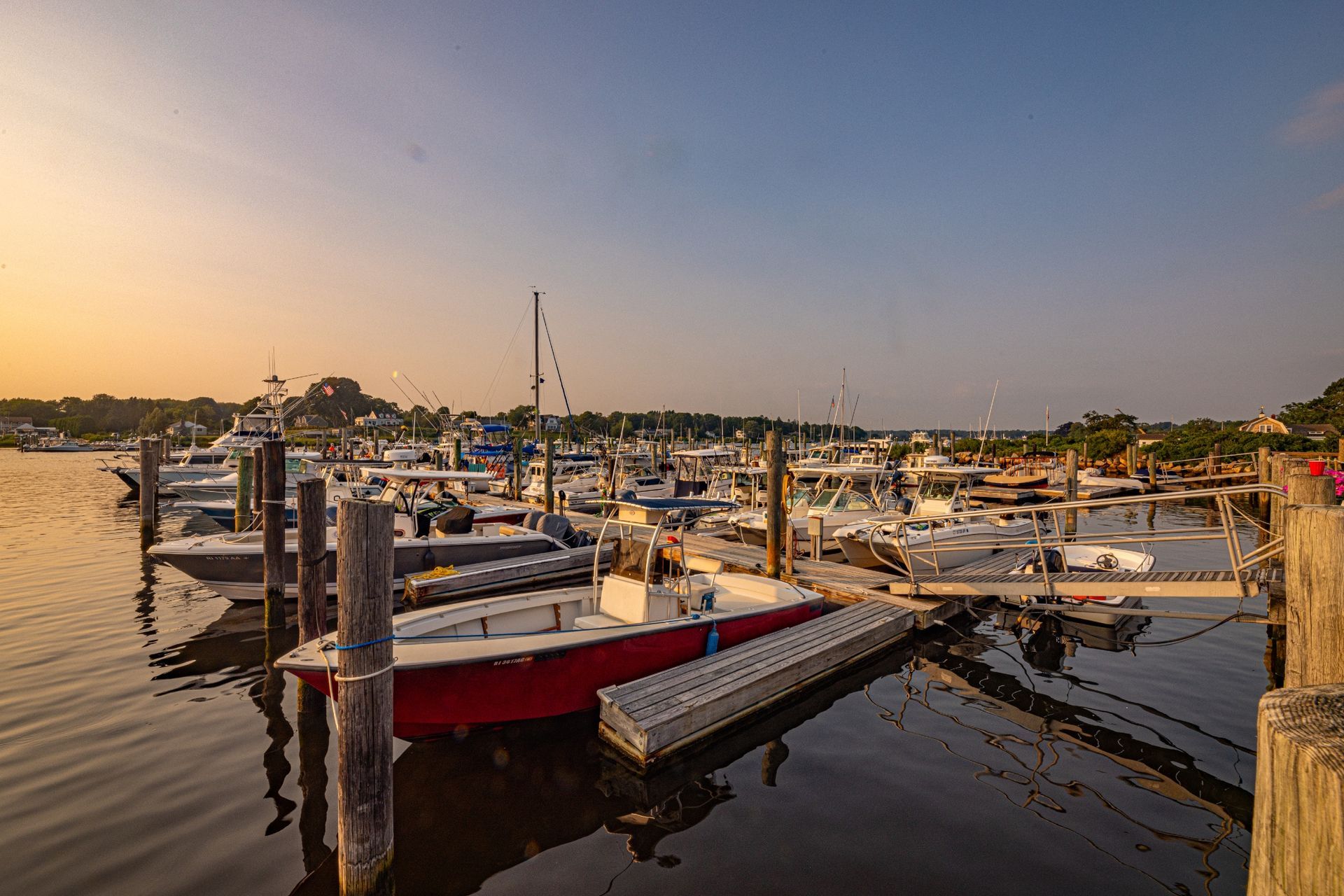 A row of boats are docked at a marina at sunset.