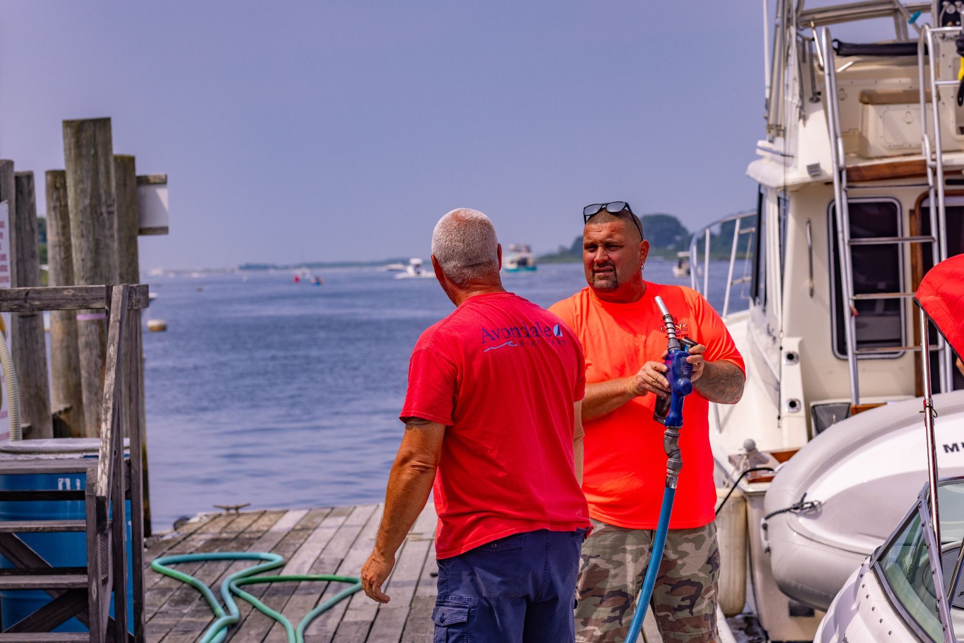 Two men are standing on a dock next to a boat talking to each other.
