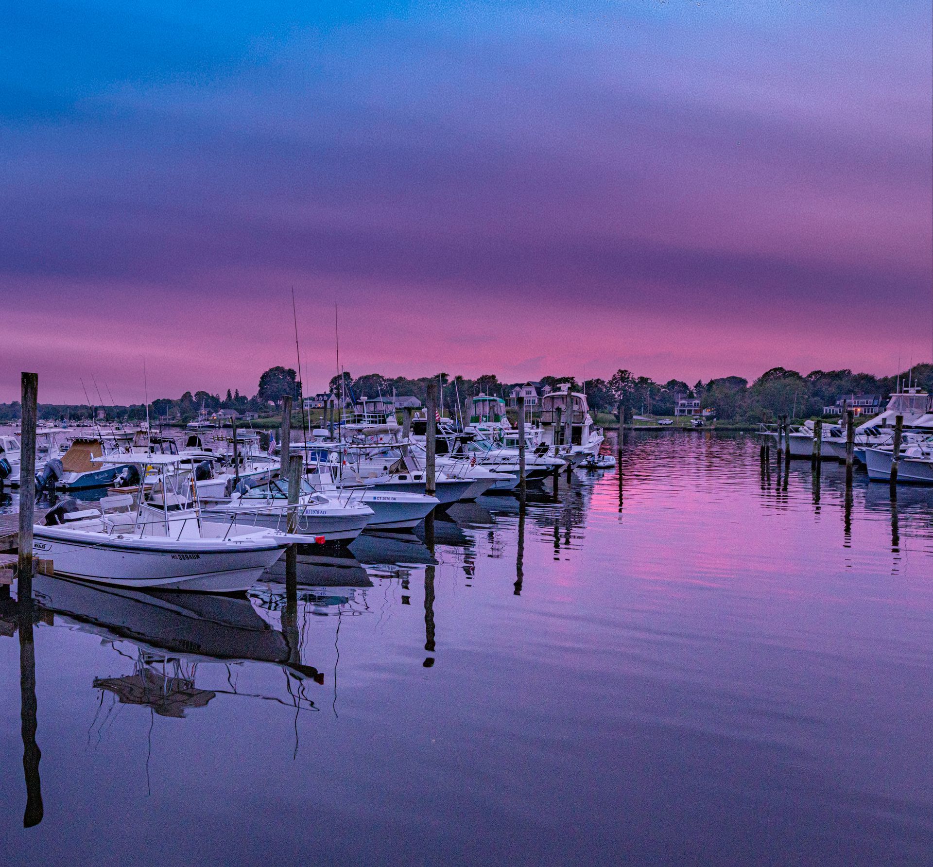 Boats docked in a calm marina at sunset, with pink and purple reflections on the water.