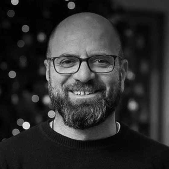 A man with a beard and glasses is smiling in a black and white photo.
