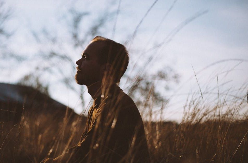 Man looking up, silhouetted in a field of tall grass during golden hour.