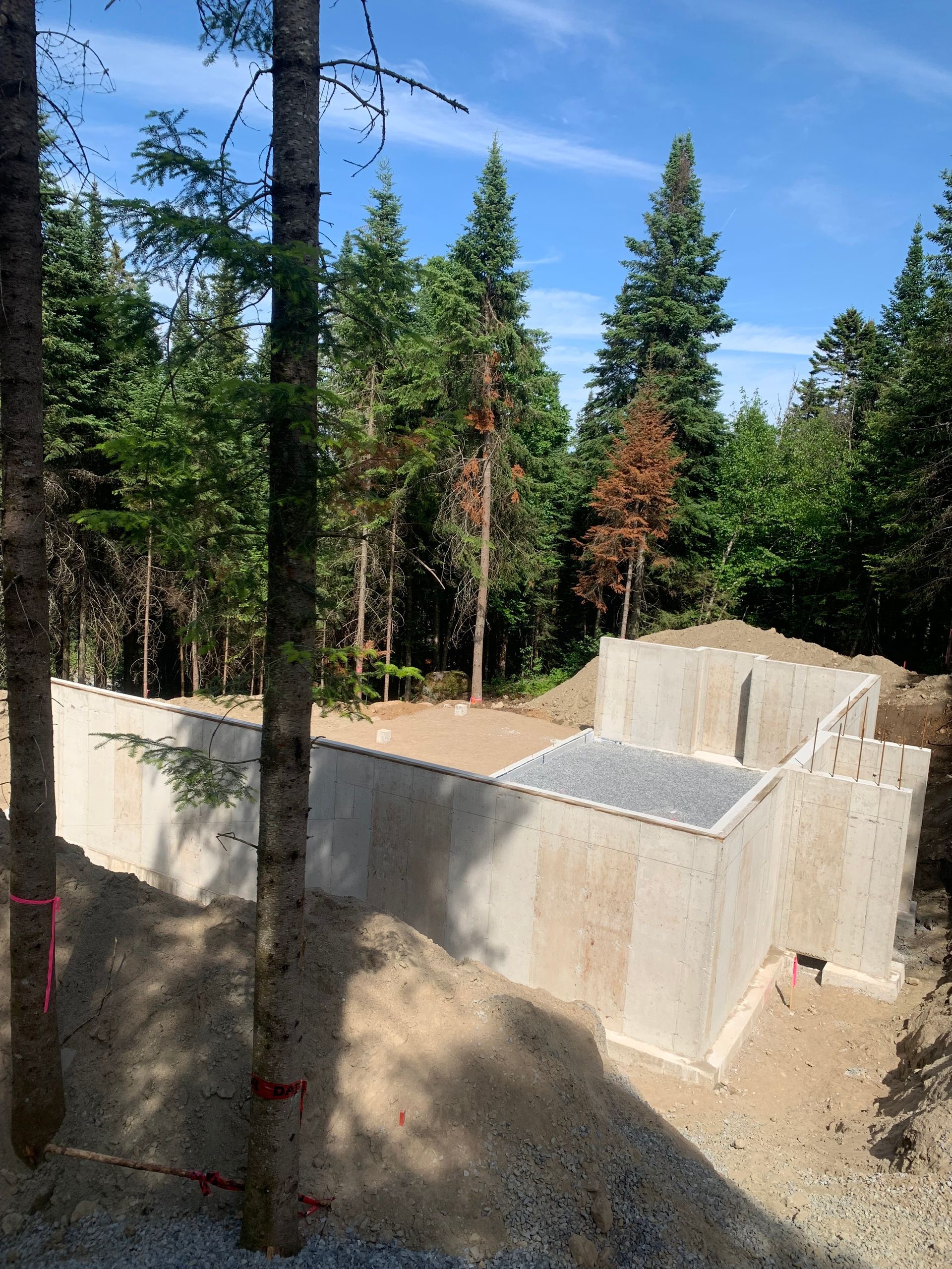 Fondations d'un bâtiment en construction, entourées d'arbres et de terre.