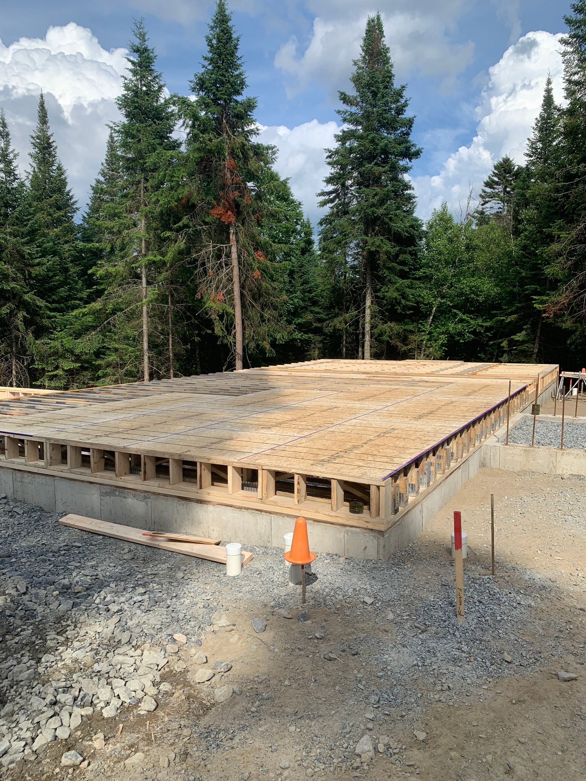 Plancher en bois sur fondations en béton, entouré de gravier et d'arbres.