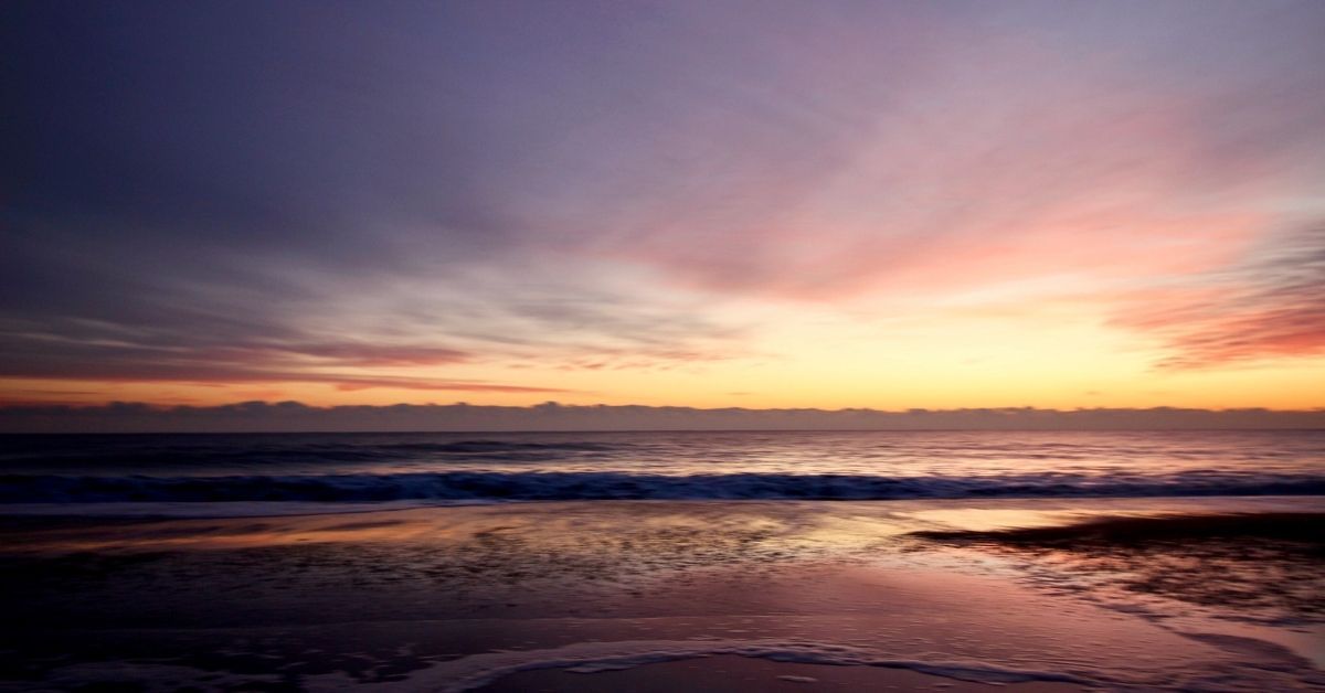 A serene winter sunrise over the Atlantic Ocean at Carolina Beach, with soft pink and orange hues reflected on the water.