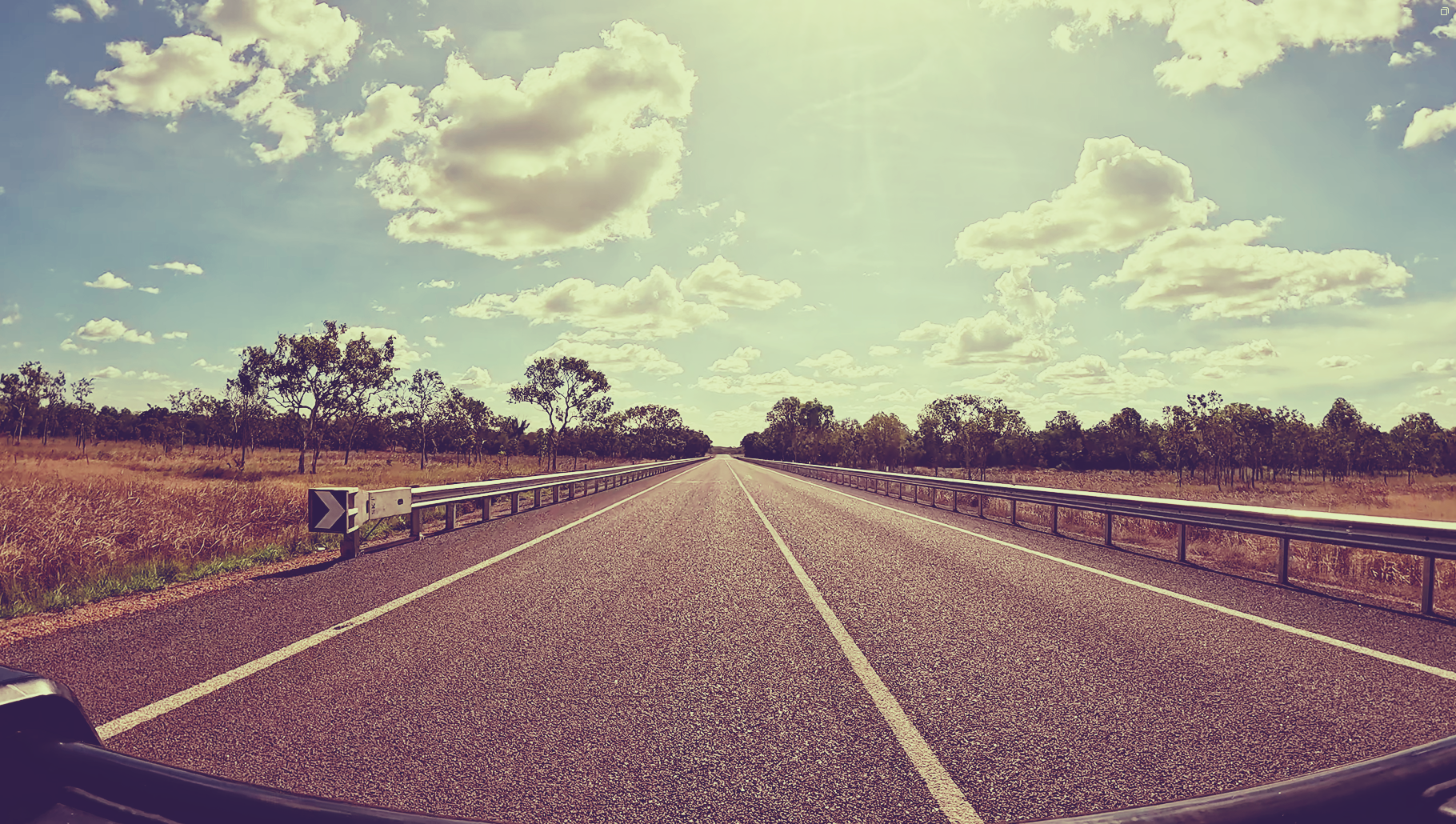 Empty rural highway stretching into the distance under a cloudy sky, seen from the center lane.