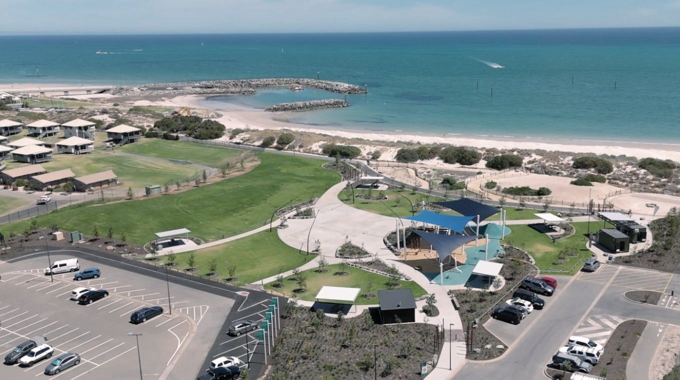 Aerial view of a beach resort with pools, parking lot, green lawns, and a sandy shoreline by blue sea