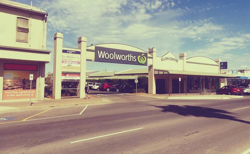 Woolworths storefront with parking lot and road in front, under a bright sky