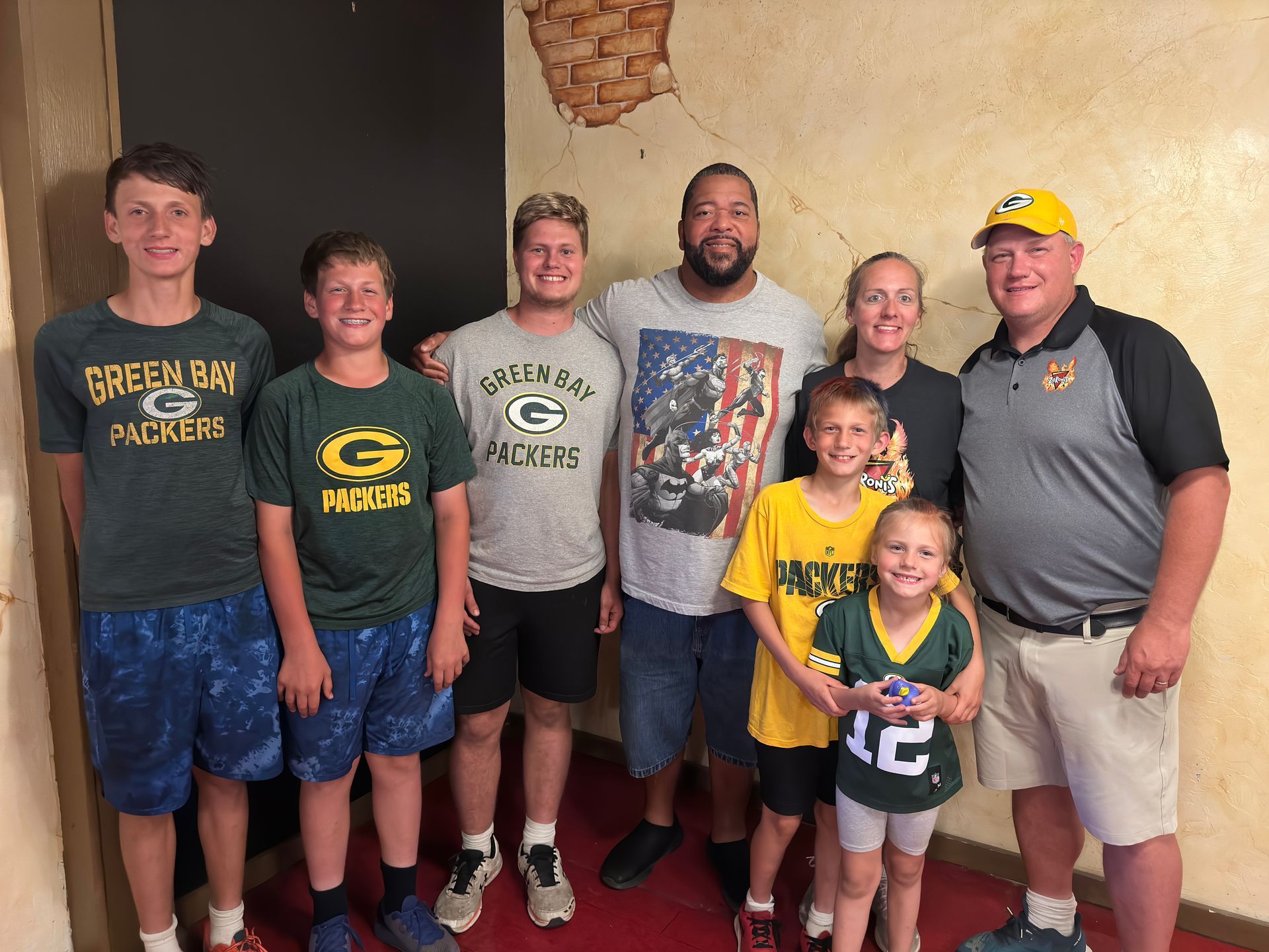 Family posing together, mostly wearing green and gold Packers gear.  Standing in a room with textured walls.