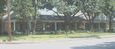 Single-story building with a dark roof, trees, and a grassy front along a road