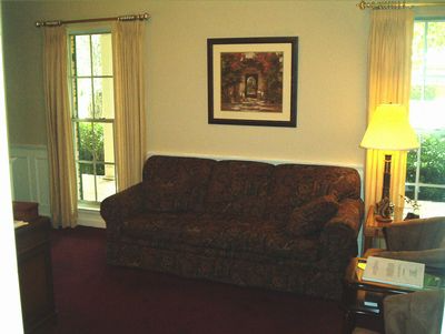 Living room with a dark couch, framed wall art, tall lamp, and windows with curtains.