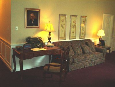 Cozy living room with patterned sofa, wooden desk, lamps, framed art, and staircase