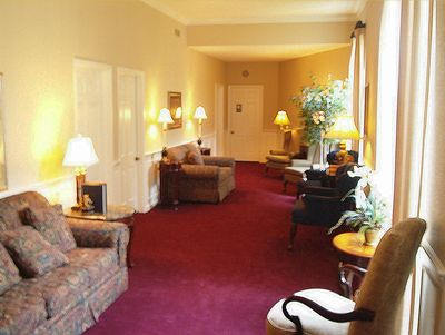 Warmly lit hotel lounge with patterned sofas, chairs, lamps, and red carpet along a long hallway.