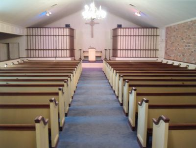 Empty church sanctuary with pews, blue carpeted aisle, chandeliers, and altar at the front