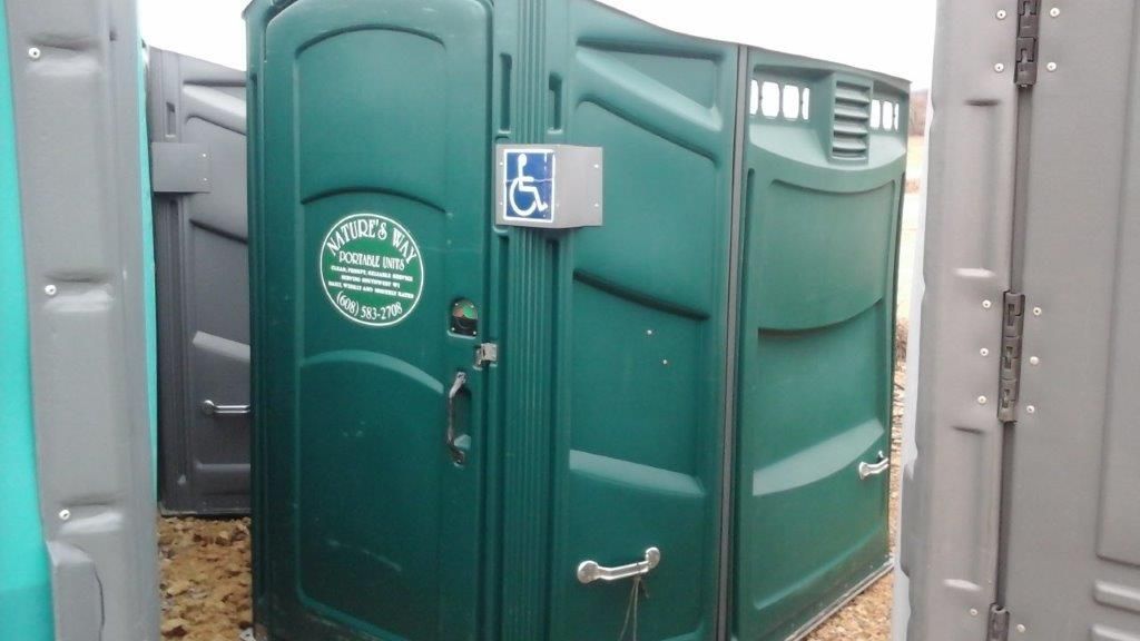 A green portable toilet with a handicap sign on the door