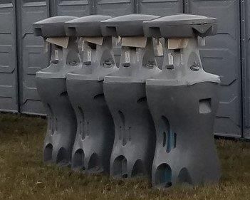 A row of portable toilets are lined up in a row in the grass