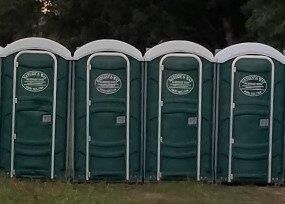 A row of green portable toilets are lined up in a field