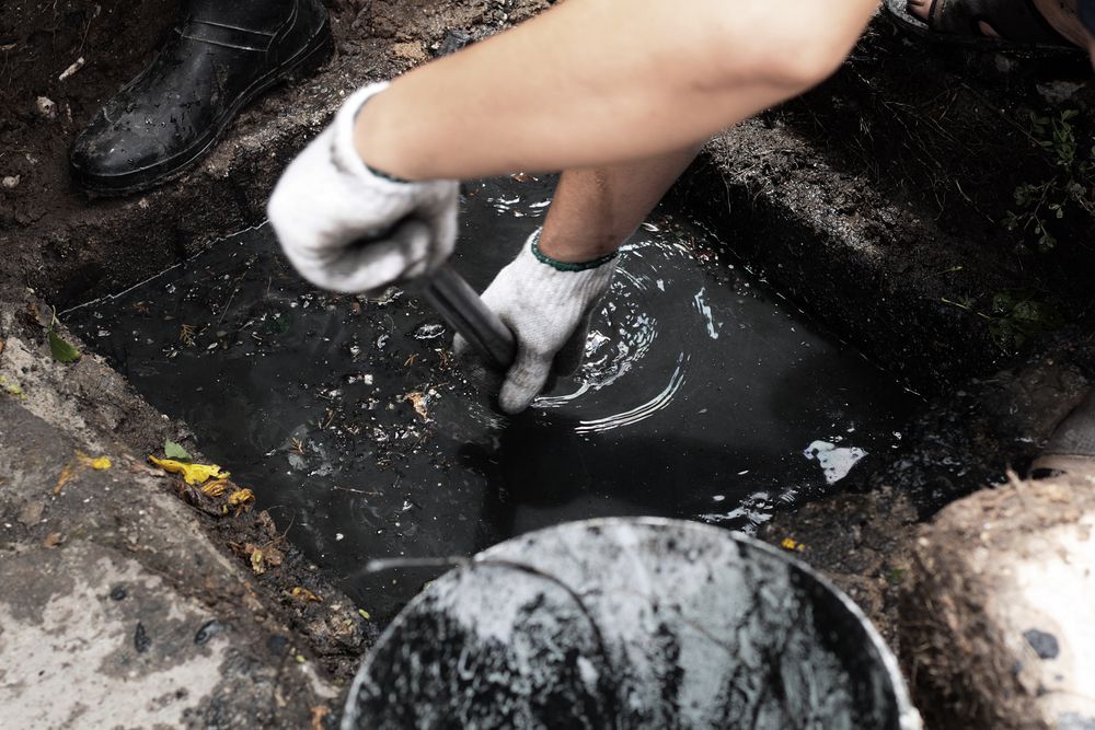 Person Reaches Into a Dark Puddle or Drain with Gloved Hands on A Wet — Tamworth Septic & Liquid Waste in Gunnedah, NSW