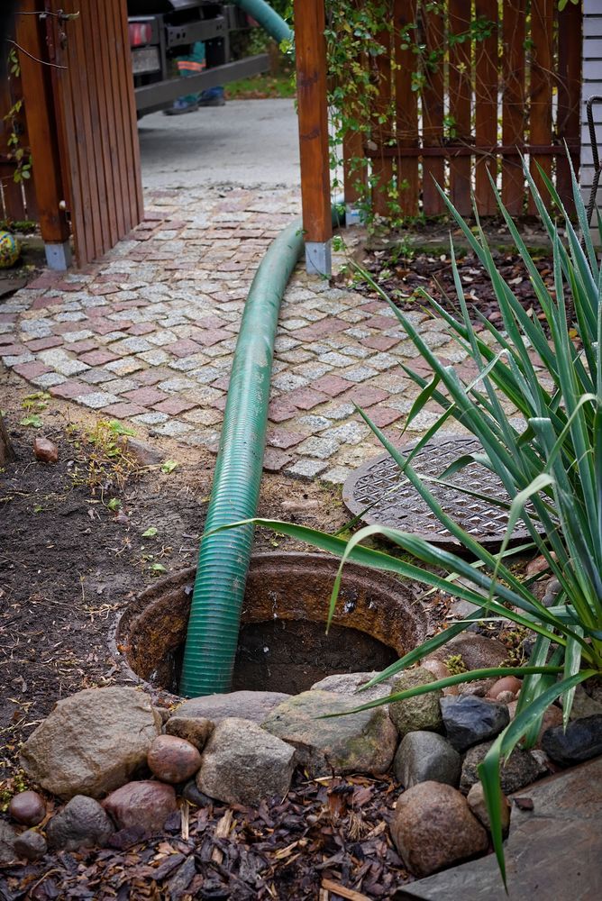 Hose Running Into a Circular Stone Lined Ground Opening Beside a Brick Path — Tamworth Septic & Liquid Waste in Duri, NSW