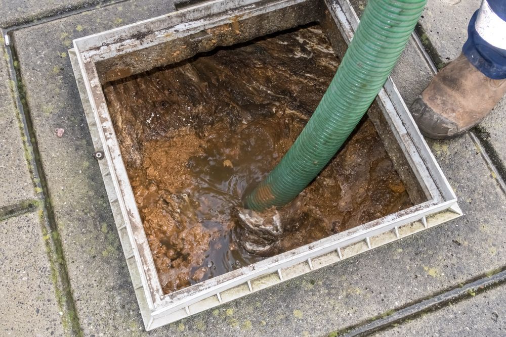 Green Hose Draining Muddy Water from A Square Outdoor Drain Cover — Tamworth Septic & Liquid Waste in Manilla & Barraba, NSW