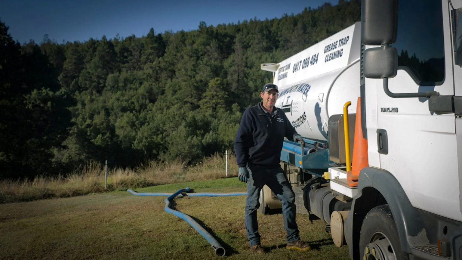 Worker Beside White Utility Truck with Hose on Grassy Roadside Near Woods — Tamworth Septic & Liquid Waste in Quirindi, NSW