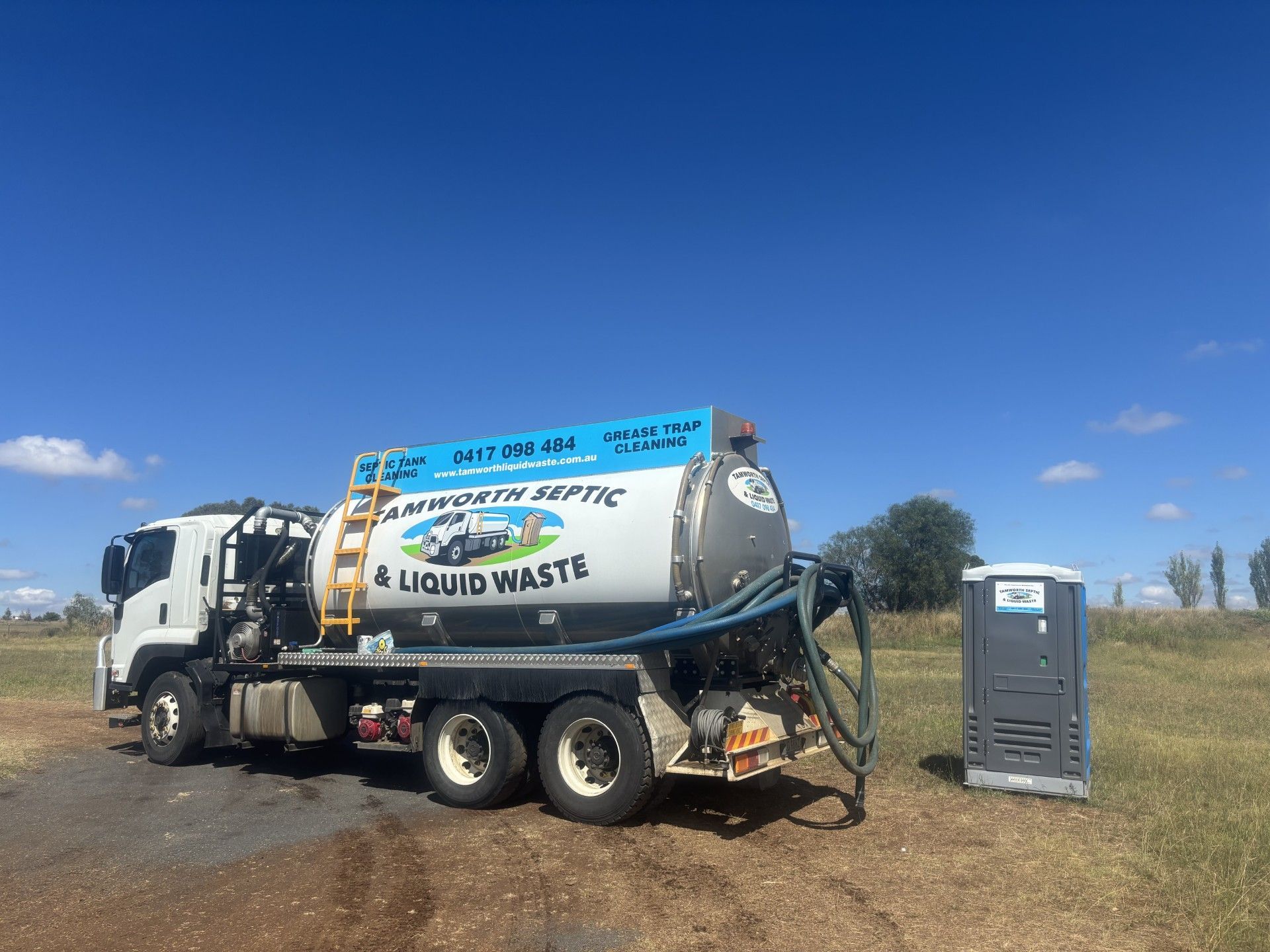 Worker Beside White Utility Truck with Hose on Grassy Roadside Near Woods — Tamworth Septic & Liquid Waste in Duri, NSW