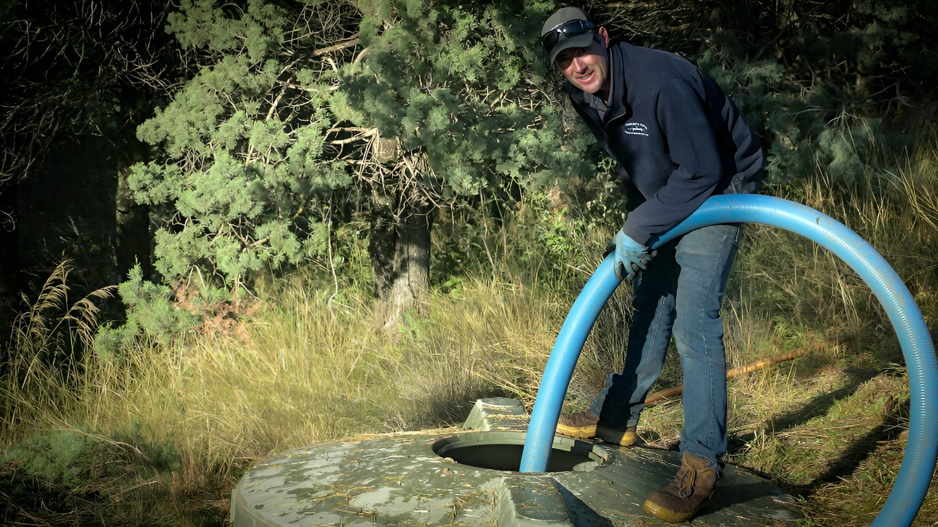 Person in Dark Clothing and Cap Stands by A Large Blue Pipe — Tamworth Septic & Liquid Waste in Gunnedah, NSW
