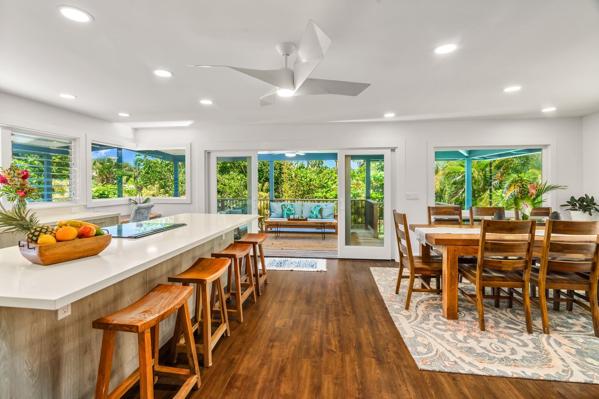 Open-plan kitchen with island, stools, dining table, and sliding doors to a patio with lush greenery.