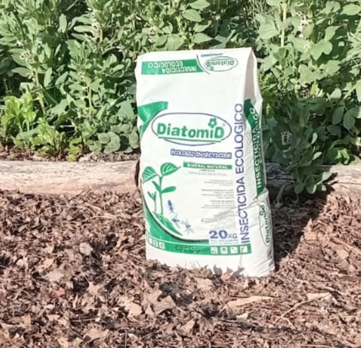 Bolsa de producto Diatomo colocada sobre tierra al aire libre frente a plantas verdes.