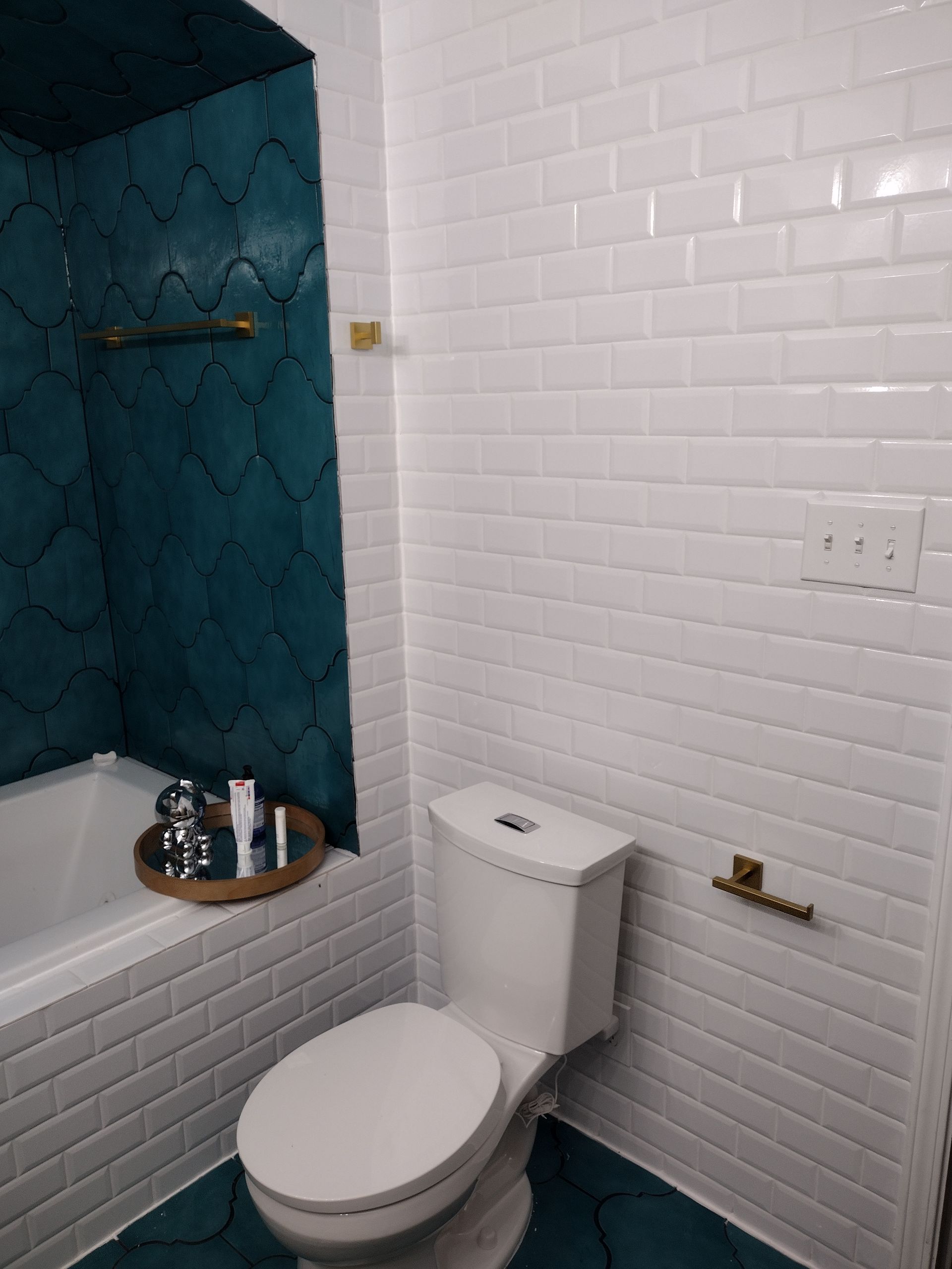 Bathroom with white subway tiles and teal accent wall. Toilet and gold fixtures are visible.