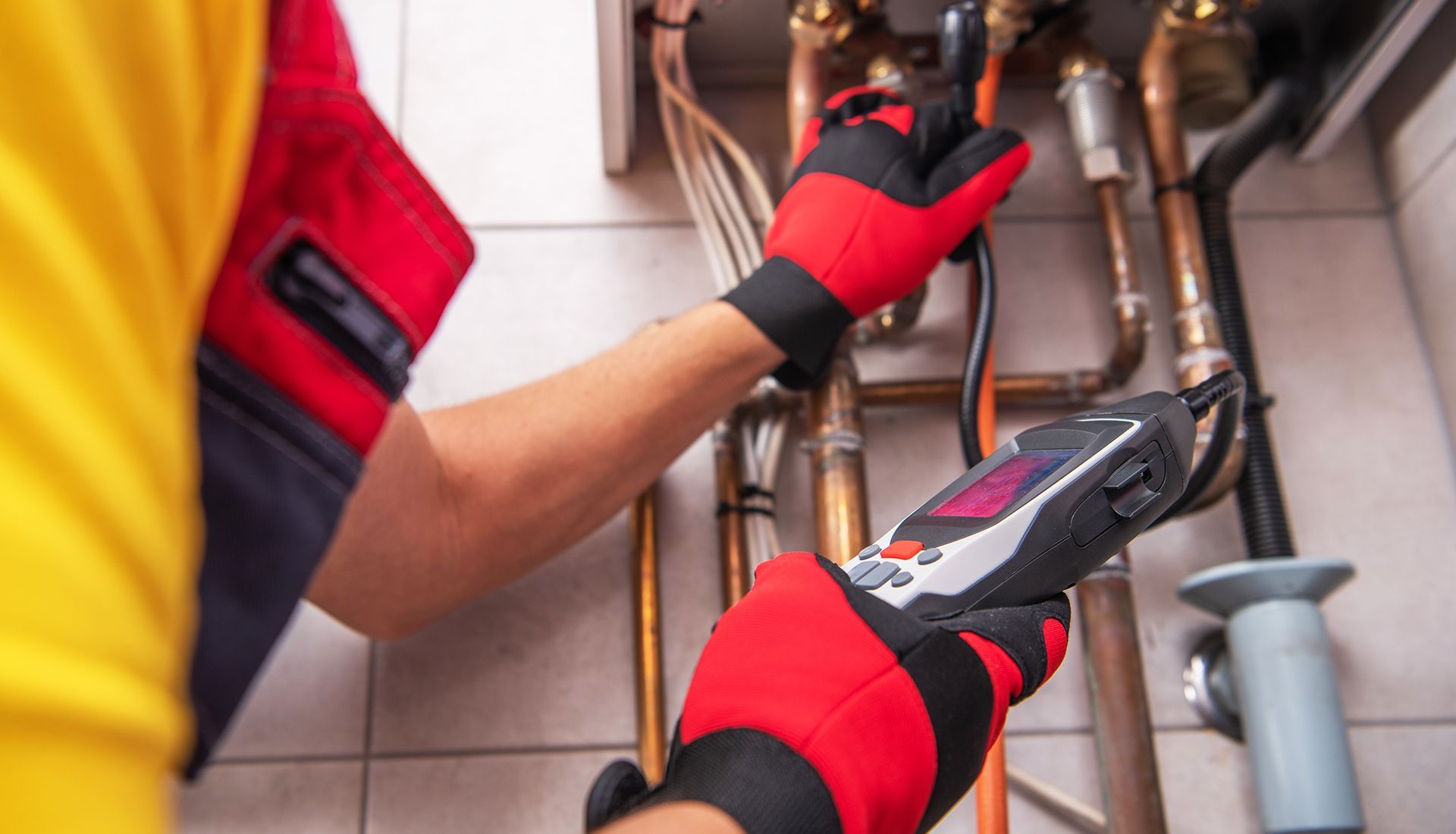 Plumber in red gloves uses a digital inspection camera to inspect pipes under a sink
