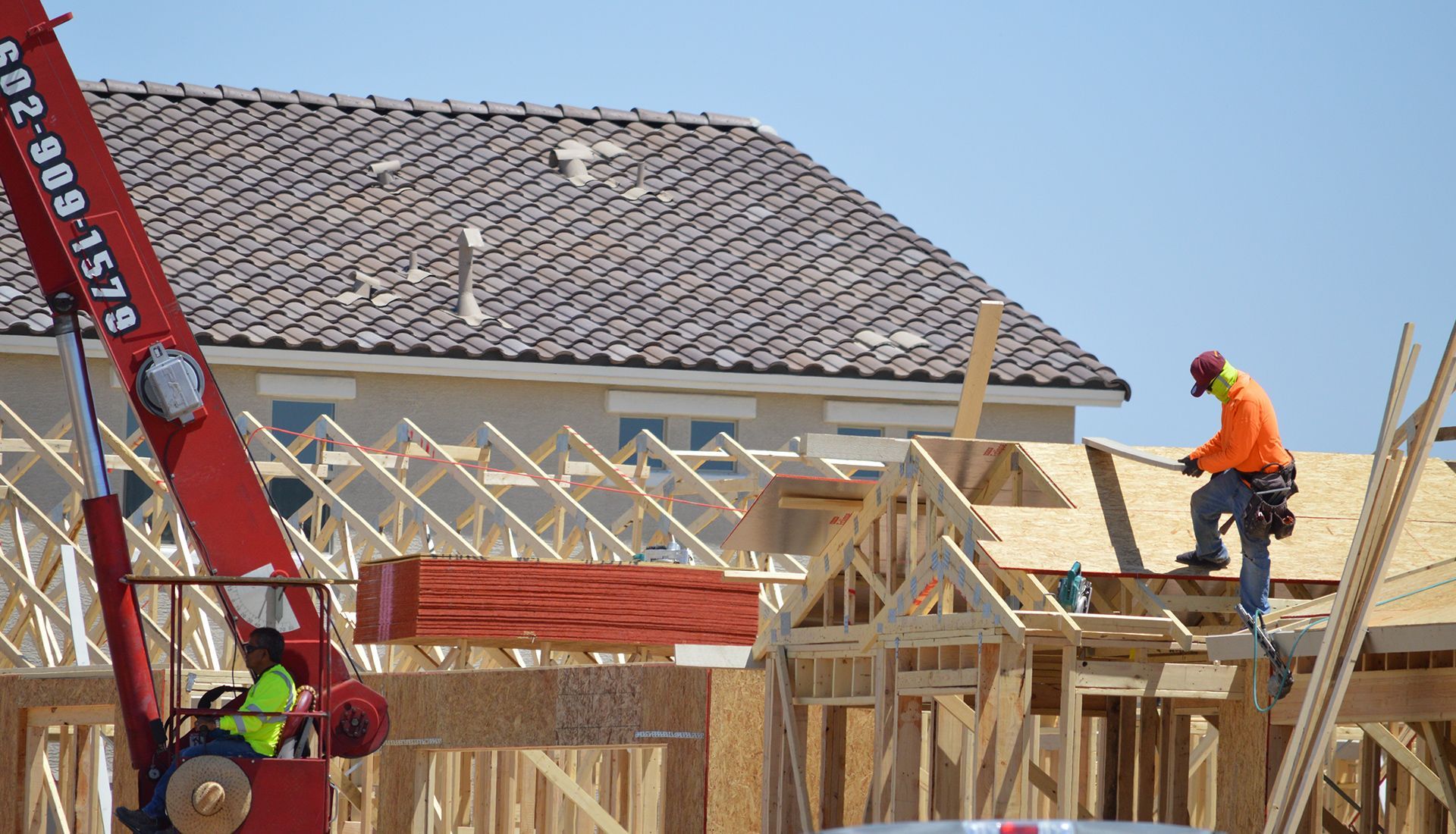 Construction workers framing a house roof with a red ladder and exposed wooden beams under a clear sky