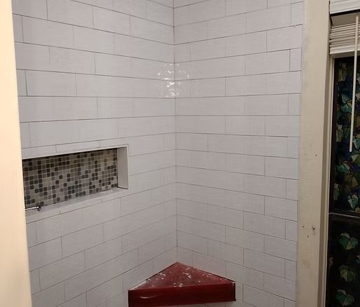 White tiled shower with a niche and red corner shelf.